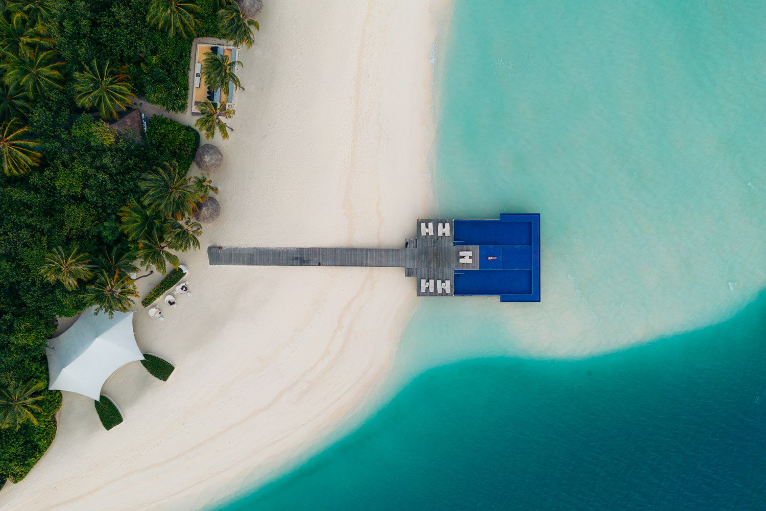 Bird's eye view of Lauren lying down in shallow square spa pool that sits offshore a white sand beach and overwater in a pristine turquoise reef. This is the quiet pool at Conrad Maldives and makes for the perfect rest spot for couples on their honeymoon vacation!