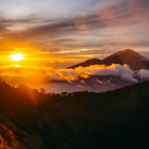 A vibrant sunrise emitting over the view of Lake Batur, Mount Abang and Mount Agung in Bali from the summit of Mount Batur. You can see the silhouette of hikers taking the view along the crater ridgeline.